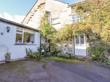 Exterior of a cottage with stone and white walls and plants around the entrance at Yanway Cottage Troutbeck near Troutbeck Bridge