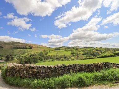 A rural landscape with a stone wall in the foreground and green hills under a blue sky with clouds at Yanway Cottage in Troutbeck near Troutbeck Bridge