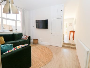 A living room with green sofas and colorful cushions a wall-mounted TV and a round rug at Flat 1 in Hunstanton