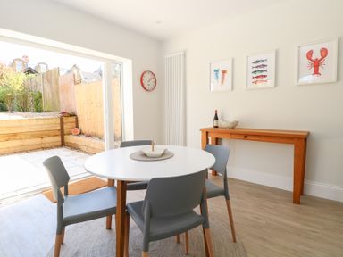 A dining area with a round table and four chairs next to sliding glass doors and a wooden console table on the side at Flat 1 in Hunstanton
