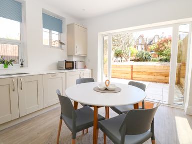 A kitchen with a round white table and four gray chairs next to sliding glass doors opening to a garden at Flat 1 in Hunstanton
