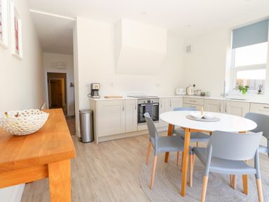A kitchen with a round dining table and chairs a wooden side table and kitchen appliances at Flat 1 in Hunstanton
