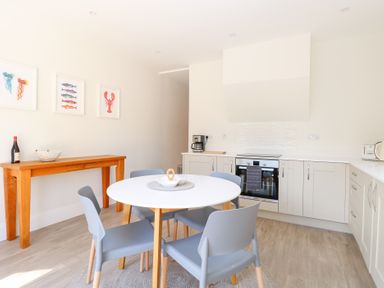 A kitchen with white cabinets a round dining table with four gray chairs and a wooden console table with a bottle and bowl on it at Flat 1 in Hunstanton