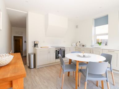 A kitchen with white cabinets a round white table and four gray chairs at Flat 1 in Hunstanton