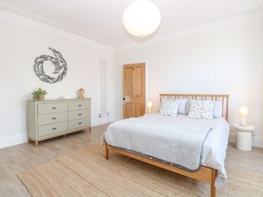 A bedroom with a wooden bed frame a dresser with decorative items and a circular wall art at Flat 1 in Hunstanton