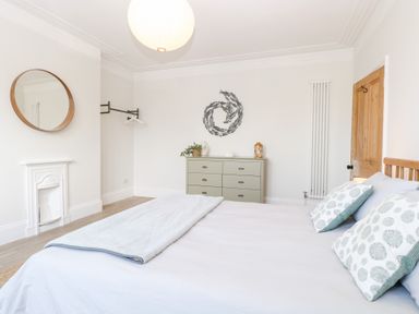 A bedroom with a bed two pillows a round mirror a dresser and a door at Flat 1 in Hunstanton