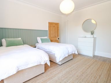 A bedroom with two single beds a white chest of drawers round mirror and a door at Flat 1 in Hunstanton
