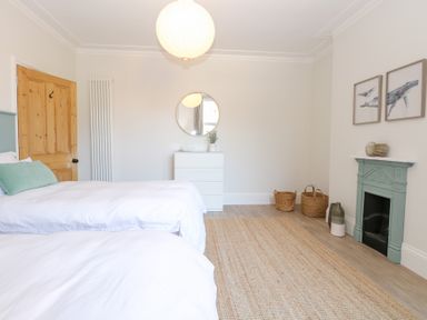 A bedroom with two beds a wooden door a dresser a round mirror a green fireplace and baskets on the floor at Flat 1 in Hunstanton