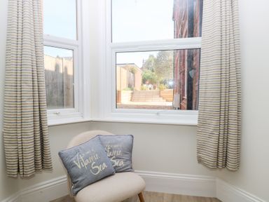 A corner with a chair and two pillows in front of two windows with striped curtains at Flat 1 in Hunstanton