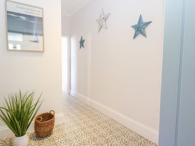 A hallway with patterned floor tiles a plant in a white pot a wicker basket a framed picture on the wall and three decorative stars on the wall at Flat 1 in Hunstanton