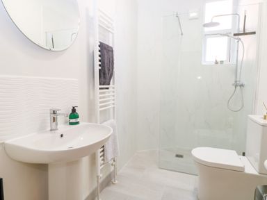 A bathroom with a pedestal sink, round mirror, towel rack with towels, walk-in shower, and toilet at Flat 1 in Hunstanton