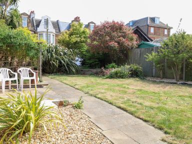 A garden with a lawn a paved pathway plants and white plastic chairs at Flat 1 in Hunstanton