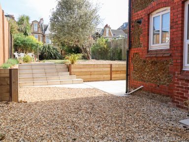 A garden with gravel pathway stairs wooden fence and plants near a brick building at Flat 1 in Hunstanton