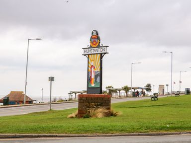 A roadside sign that says Hunstanton with a decorative panel and a coat of arms on a grassy area near the seafront at Flat 1 in Hunstanton