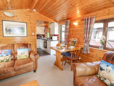 A living room with leather sofas and a wooden dining table near a kitchen at Robins Nest Number 12 Burnside Park near Keswick