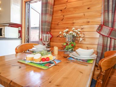 A wooden dining table set with plates glasses and cutlery beside a wooden paneled wall with flowers at Robins Nest Number 12 Burnside Park near Keswick