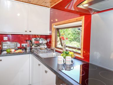 A kitchen corner with a sink, electric kettle, toaster, cutting board with food, mugs, fruit basket, and window at Robins Nest Number 12 Burnside Park near Keswick