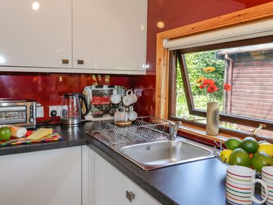 A kitchen countertop with a sink a kettle a toaster a fruit bowl and mugs by a window at Robins Nest Number 12 Burnside Park near Keswick