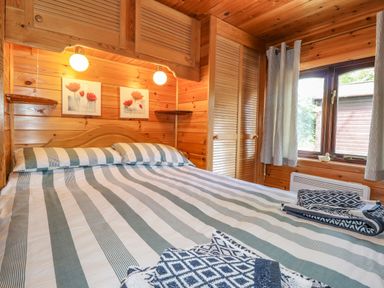 A wooden bedroom with a double bed striped bedding folded towels a window and wall cabinets at Robins Nest Number 12 Burnside Park near Keswick