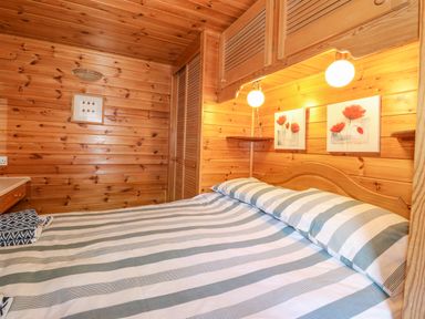 A bedroom with a striped bedspread and wooden walls at Robins Nest Number 12 Burnside Park near Keswick