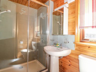 A bathroom with a shower enclosure a pedestal sink with soap a toilet and a window with striped blinds at Robins Nest Number 12 Burnside Park near Keswick