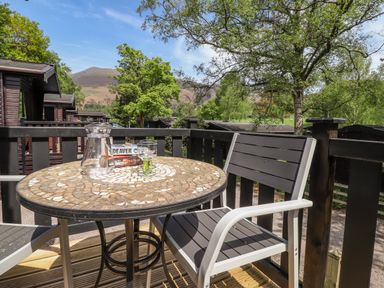 A balcony with a round mosaic table and two chairs overlooking trees and hills at Robins Nest Number 12 Burnside Park near Keswick