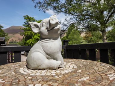 A pig statue on a mosaic table outside with trees and hills in the background at Robins Nest Number 12 Burnside Park near Keswick