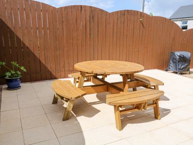 A patio area with a wooden round picnic table and benches and a brown wooden fence at Stillwaters in Bushmills County Antrim