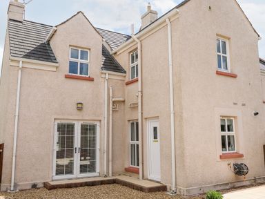 The back exterior of a beige two-story house with multiple windows and a white double door at Stillwaters Bushmills County Antrim