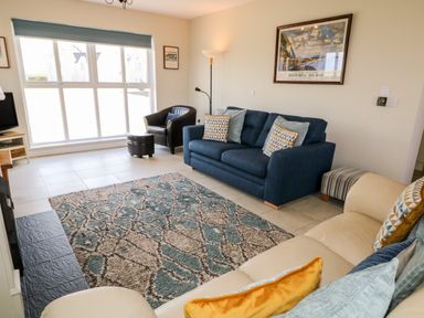 A living room with blue and beige sofas a patterned rug a black armchair a large window and a framed picture at Stillwaters in Bushmills County Antrim
