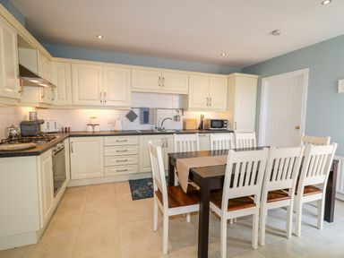 A kitchen with cream cabinets black countertop and a dark dining table with white chairs at Stillwaters in Bushmills County Antrim
