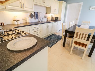 A kitchen with white cabinets a gas stove a sink a kettle a microwave and a dining table with four chairs at Stillwaters in Bushmills County Antrim