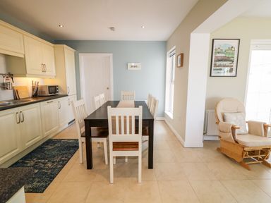 A kitchen with cream cabinets a black dining table with white chairs and a beige cushioned rocking chair at Stillwaters in Bushmills County Antrim