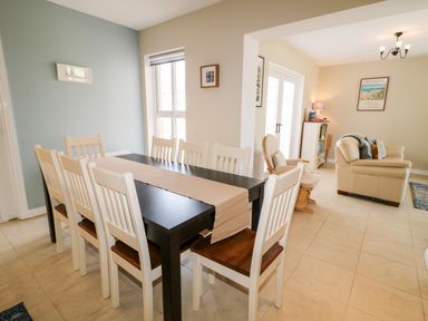 A dining area with a black table and white chairs next to a living room with beige sofas at Stillwaters in Bushmills County Antrim