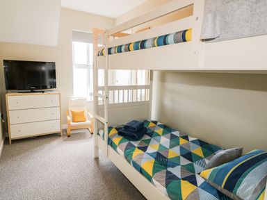 A bedroom with a bunk bed a chest of drawers with a TV and a chair with a cushion at Stillwaters in Bushmills County Antrim
