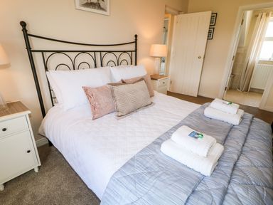 A bedroom with a bed made up with white linens and pillows bedside tables with lamps and a doorway leading to a bathroom at Stillwaters in Bushmills County Antrim