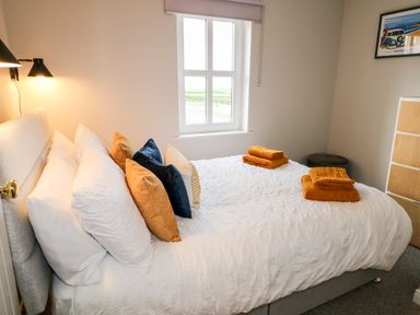 A bedroom with a bed with white sheets and multiple pillows under a window at Stillwaters in Bushmills County Antrim
