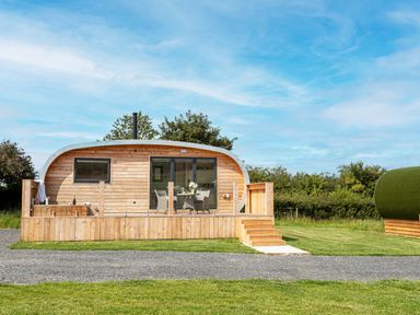 A wooden cabin with a small deck and outdoor seating in a grassy area at Low Longlands in Cartmel