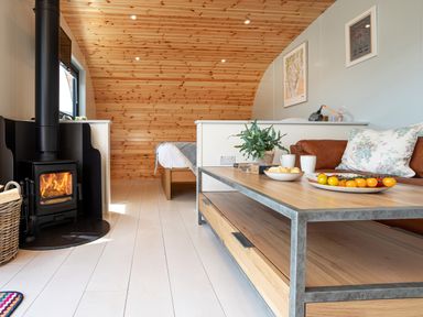 A living area with a wood burning stove a wooden coffee table with plates and a plant and a bed in the background at Low Longlands in Cartmel