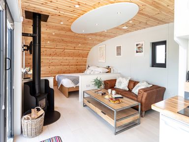 A living area with a brown leather sofa and wooden coffee table near a bed and a wood stove at Low Longlands in Cartmel