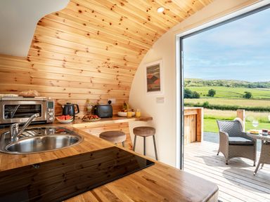 A small kitchen with wooden counters and walls a stool and a door opening to an outdoor patio with a chair and table at Low Longlands in Cartmel
