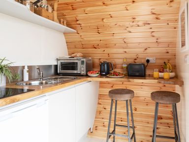 A kitchen with a wooden countertop a metal sink two stools a toaster kettle oven and fruits at Low Longlands in Cartmel