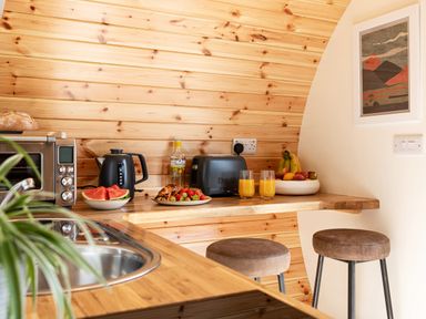 A kitchen counter with a toaster kettle plates of fruit two stools and a framed picture on the wall at Low Longlands in Cartmel