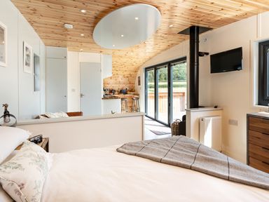 A bedroom with a bed and blanket looking out to a kitchen area with stools and sliding glass doors at Low Longlands in Cartmel