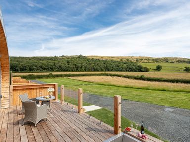A wooden deck with a table and two chairs overlooking grassy fields and hills at Low Longlands in Cartmel