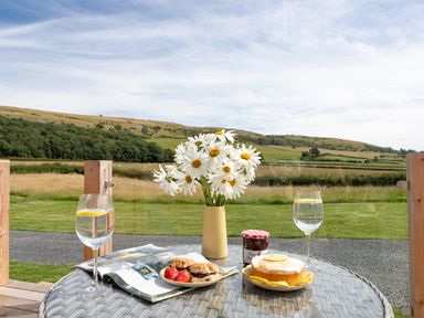 A patio table with flowers water glasses scones strawberries cake and jam with a countryside view at Low Longlands in Cartmel