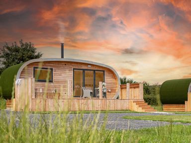A wooden pod with a deck and chairs under a colorful sky at Low Longlands in Cartmel