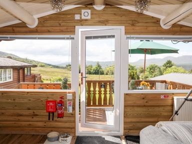 A wooden room with a glass door leading to a balcony and outdoor umbrella at Ty Coed - 63 in Bronaber near Trawsfynydd