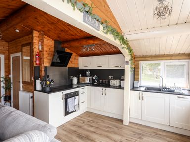 A kitchen with white cabinets black countertops and wooden walls with a window above the sink at Ty Coed - 63 in Bronaber near Trawsfynydd