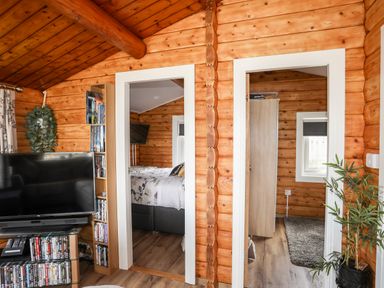 A wooden interior with a tv and dvd shelves next to two doorways showing a bedroom and another room with a wardrobe at Ty Coed - 63 in Bronaber near Trawsfynydd